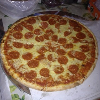 A pizza photographed on a phone on a busy table, flat and dim.